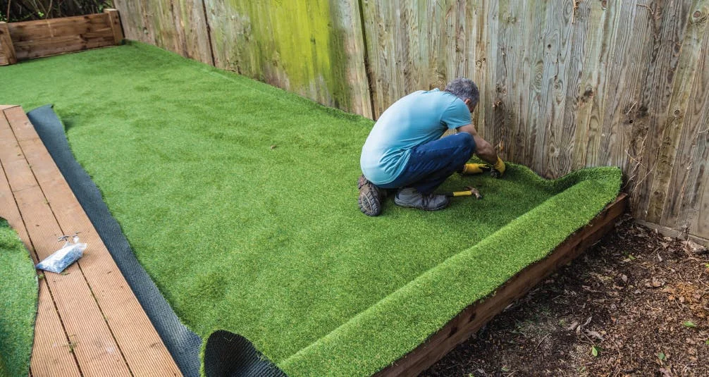 Landscaper install artificial grass beside wooden fence